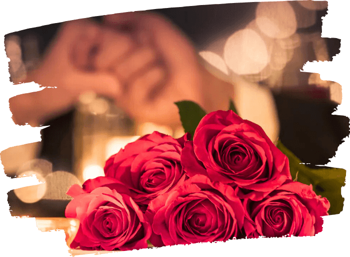 Close-up of a bouquet of red roses with a blurred person resting their head on their hand in the background.